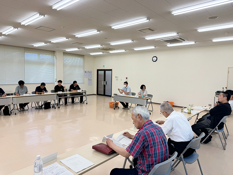 コの字型に机が並べられ、多くの関係者が集まって真剣に話し合っている会議の様子。